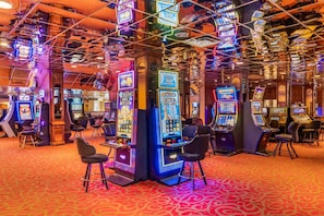 Um cassino com máquinas caça-níqueis, banquetas de bar e um tapete estampado.