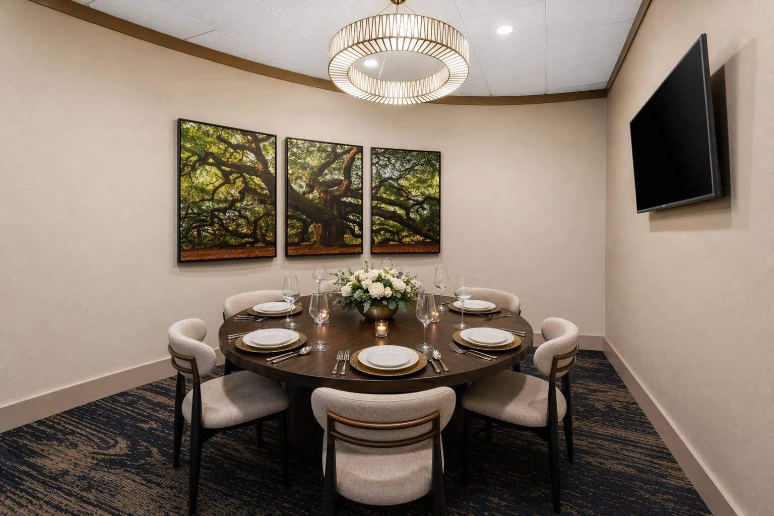 A conference room with a round table set for six, surrounded by six chairs, a chandelier, and three framed artworks on the wall.