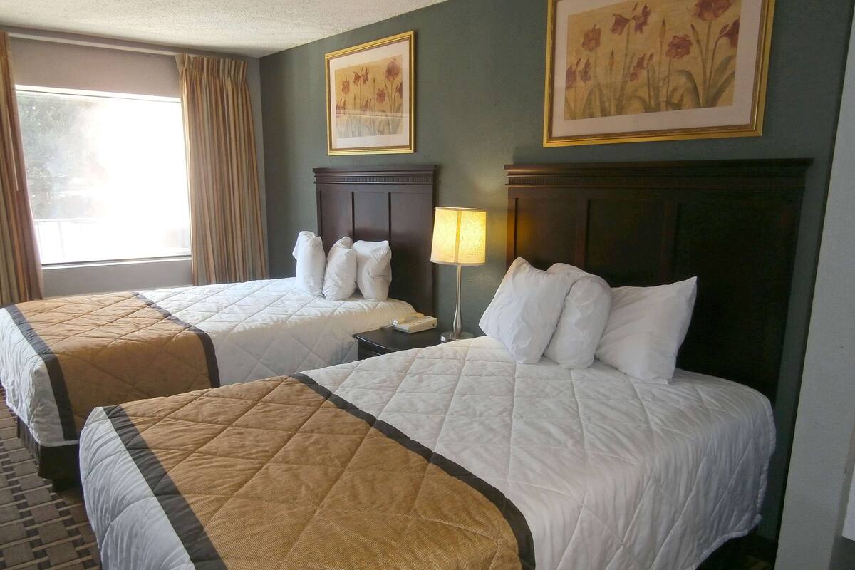 Een hotelkamer met twee bedden, een nachtkastje, een lamp en twee lijstjes met bloemstillevens aan de muur.