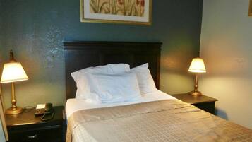 A neatly made bed with white linens, two bedside lamps, a telephone, and a framed floral artwork on the wall.
