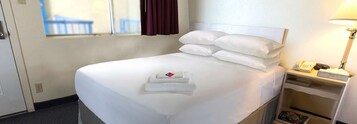 A hotel room with a bed, a bedside table with a lamp, and a window with curtains.