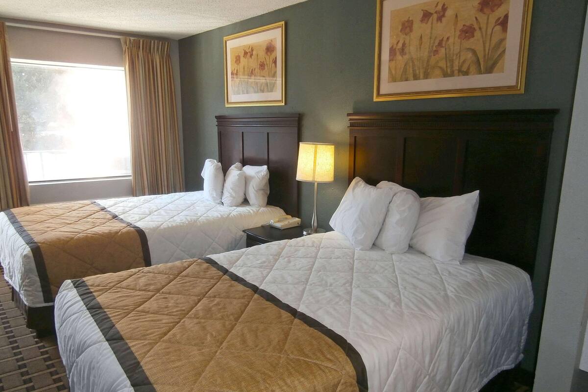 Een hotelkamer met twee bedden, een nachtkastje, een lamp en twee florale schilderijen in lijsten aan de muur.