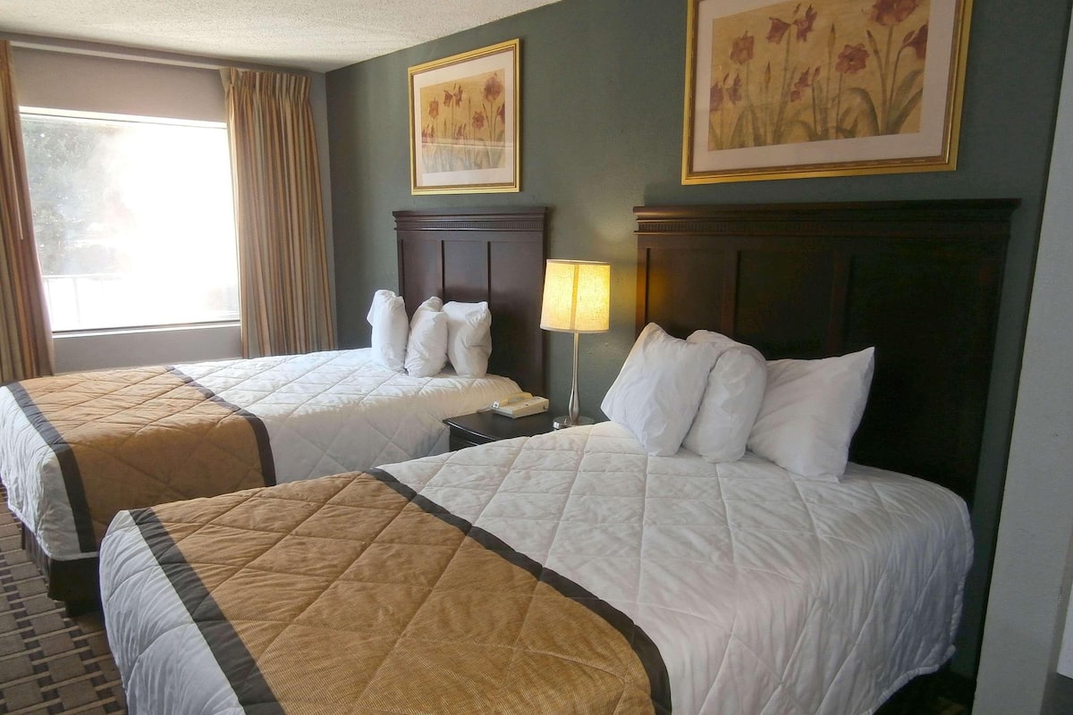 Une chambre d’hôtel avec deux lits, une table de chevet, une lampe et deux tableaux représentant des motifs floraux, encadrés et accrochés au mur.