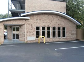 A brick building with a curved roof, a covered entrance, and a parking lot.