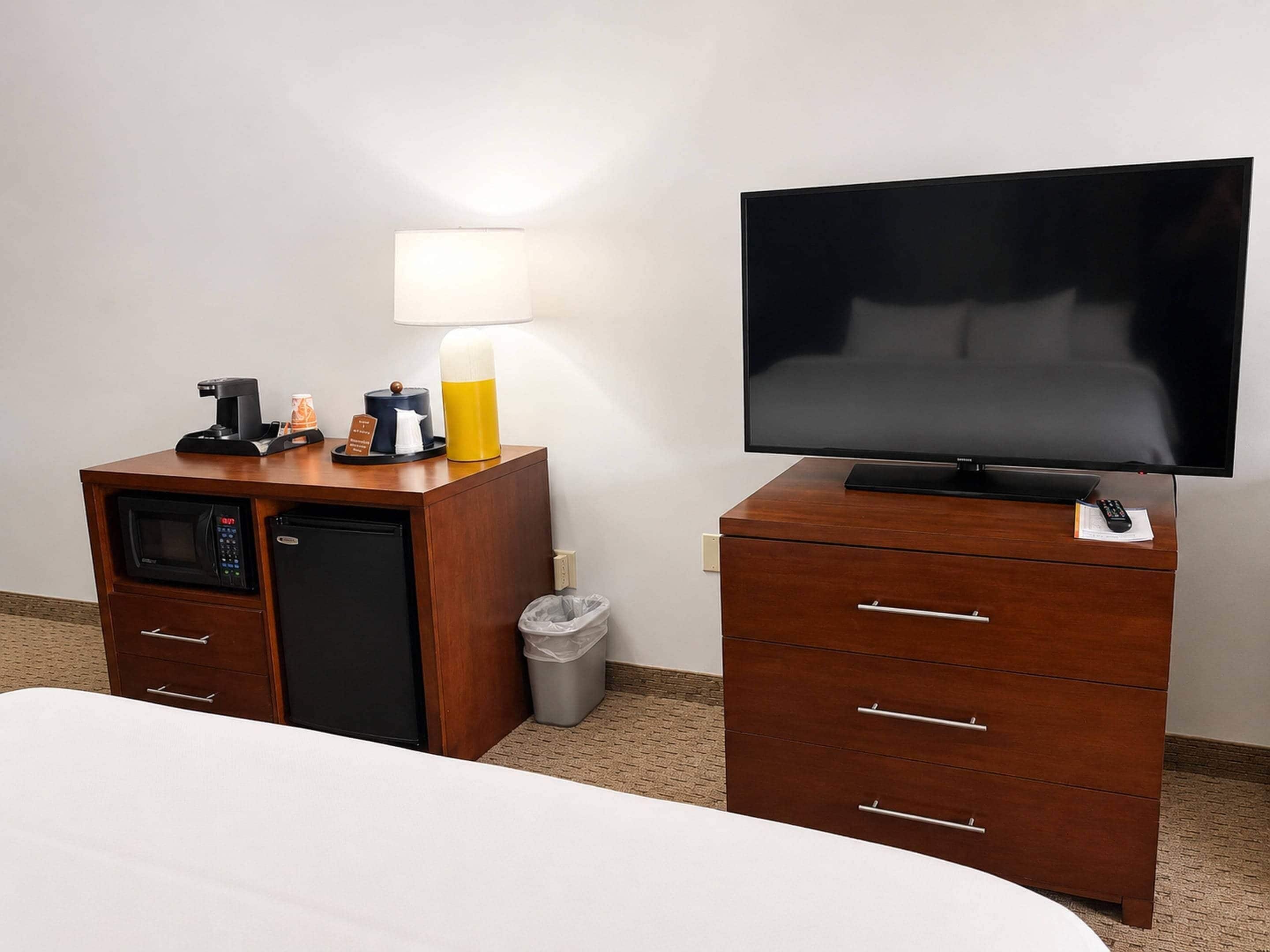 Een hotelkamer met een bed, een televisie, een minibar, een lamp en een prullenbak.
