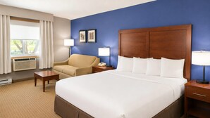 A hotel room with a large bed, a chair, a bedside table, a lamp, and a window with curtains. - Comfort Inn Iron Mountain North (Iron Mountain)