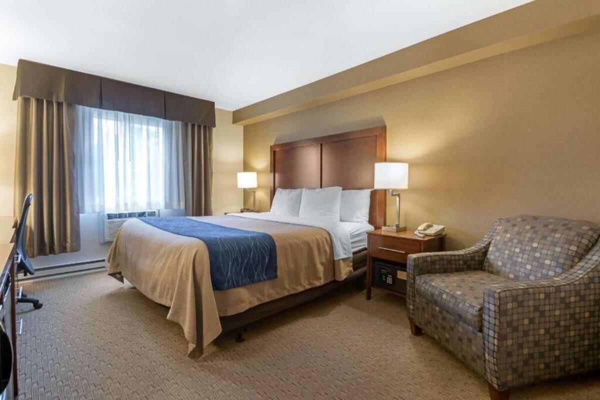 A hotel room with a bed, bedside lamps, a chair, and a desk with a phone.