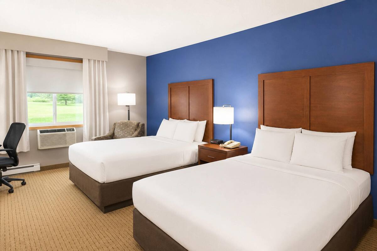 A hotel room with two beds, a desk, a chair, and a window with curtains.