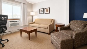 A hotel room with a beige sofa, a patterned armchair, a wooden coffee table, a black office chair, and a standing lamp. - Comfort Inn Iron Mountain North (Iron Mountain)