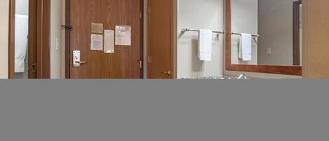 A bathroom with a wooden door, a towel rack with two white towels, and a large mirror above the sink.