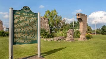 A historical marker sign with text about the Ardis Furnace, surrounded by a grassy area and stone structures.