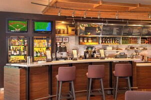 Una zona de bar con taburetes, un mostrador con la carta y estantes con botellas.