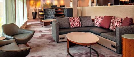 A modern hotel lobby with a sectional sofa, armchairs, a coffee table, and a fireplace.