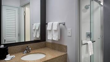 A bathroom with a granite countertop sink, a mirror, and a glass shower enclosure.