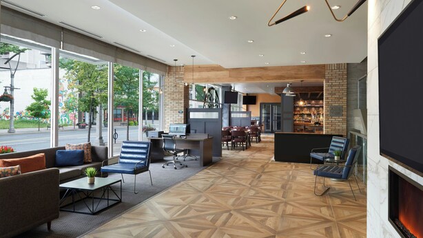 Eine großzügige Lobby mit modernem Design, inklusive einer großzügigen Sitzecke, einem Kamin und einer Bar-/Lounge-Ecke mit einer Ziegelwand.