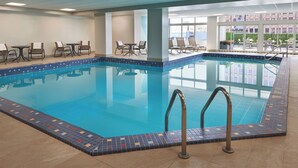 Ein Hallenbad mit klarem, blauem Wasser, umgeben von Liegestühlen und Tischen.