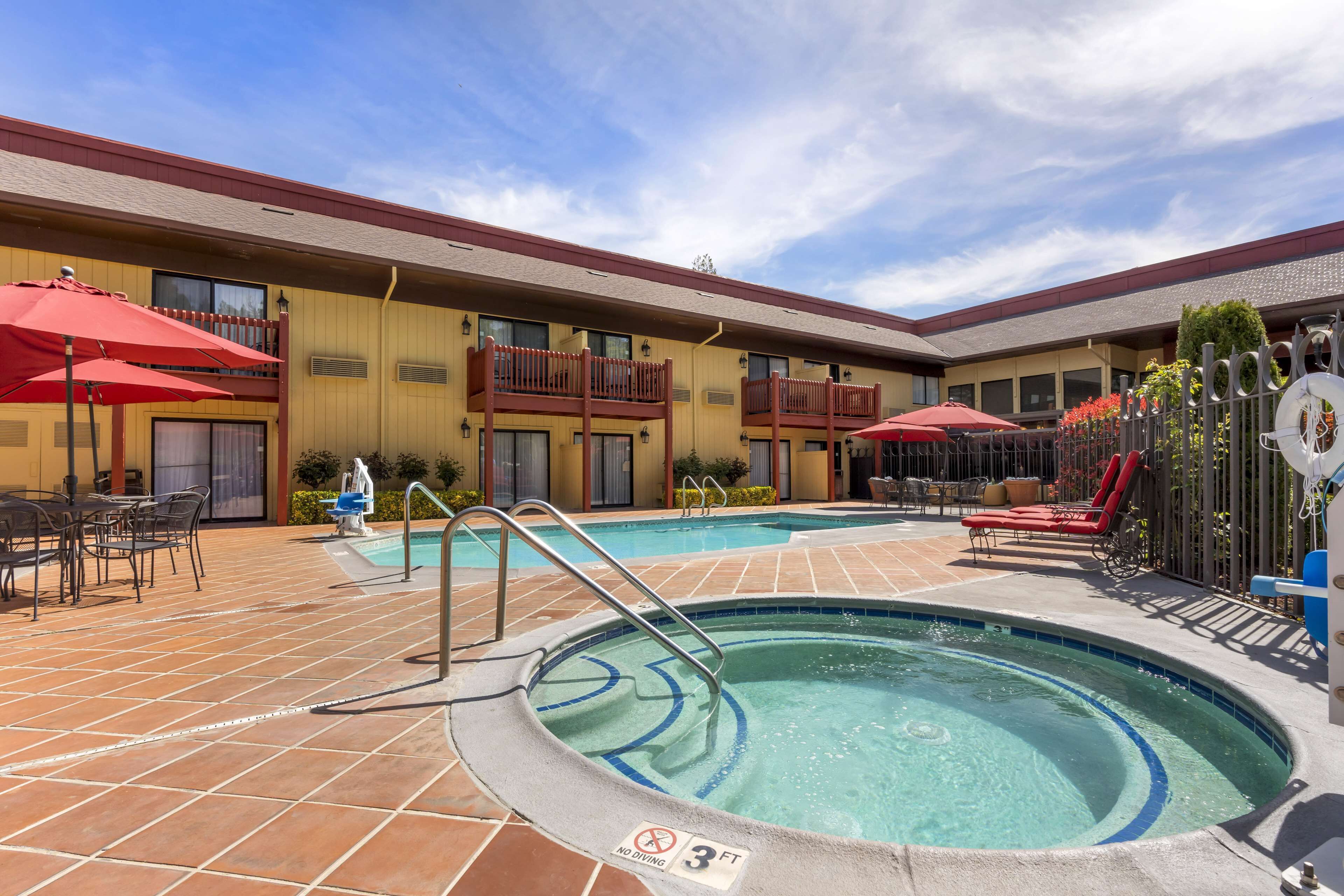 A hotel pool area with a tiled deck, lounge chairs, and umbrellas.