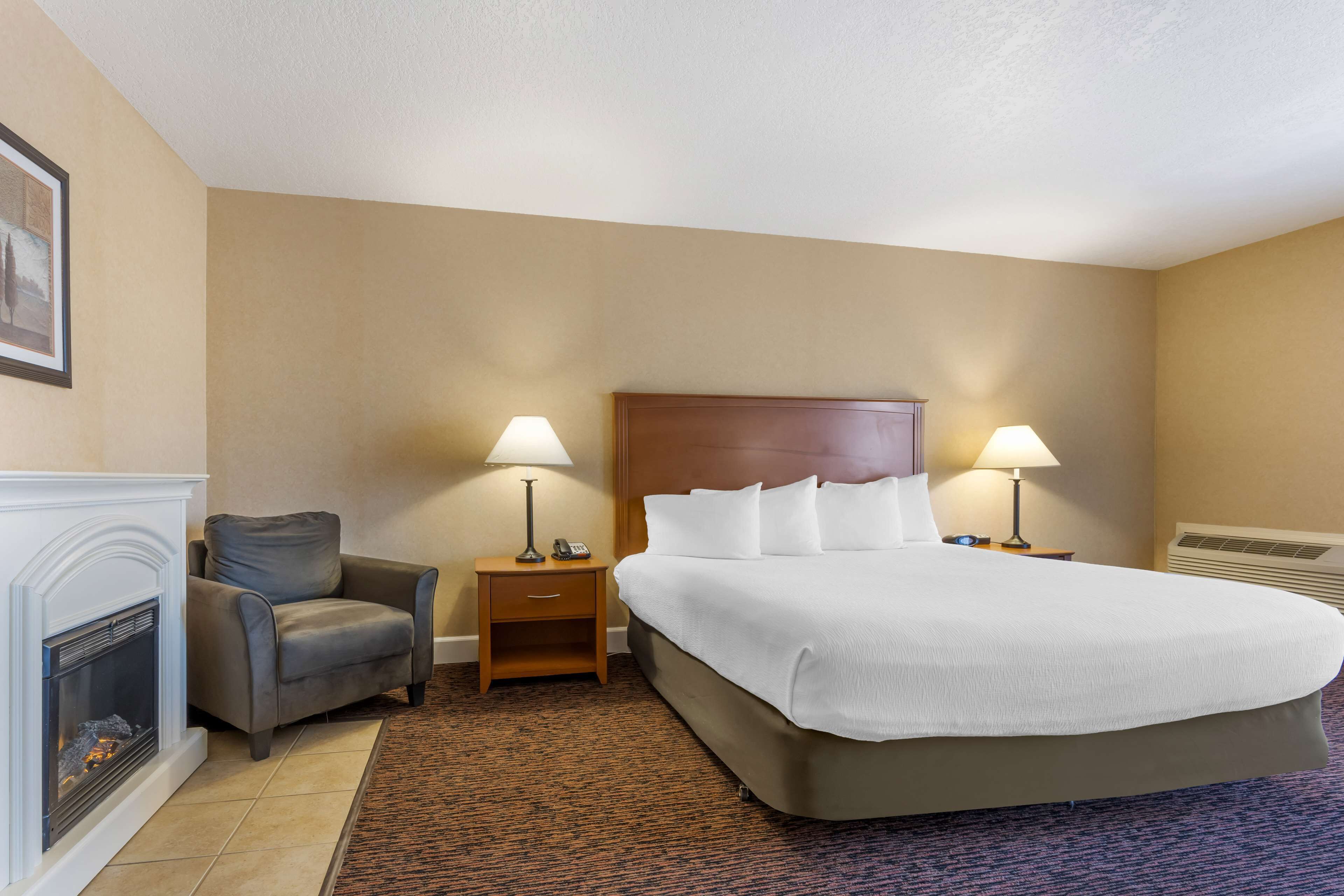 Une chambre d’hôtel avec un grand lit, deux tables de chevet avec des lampes, un fauteuil et une cheminée.