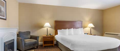 A hotel room with a large bed, two bedside tables with lamps, a chair, and a fireplace.