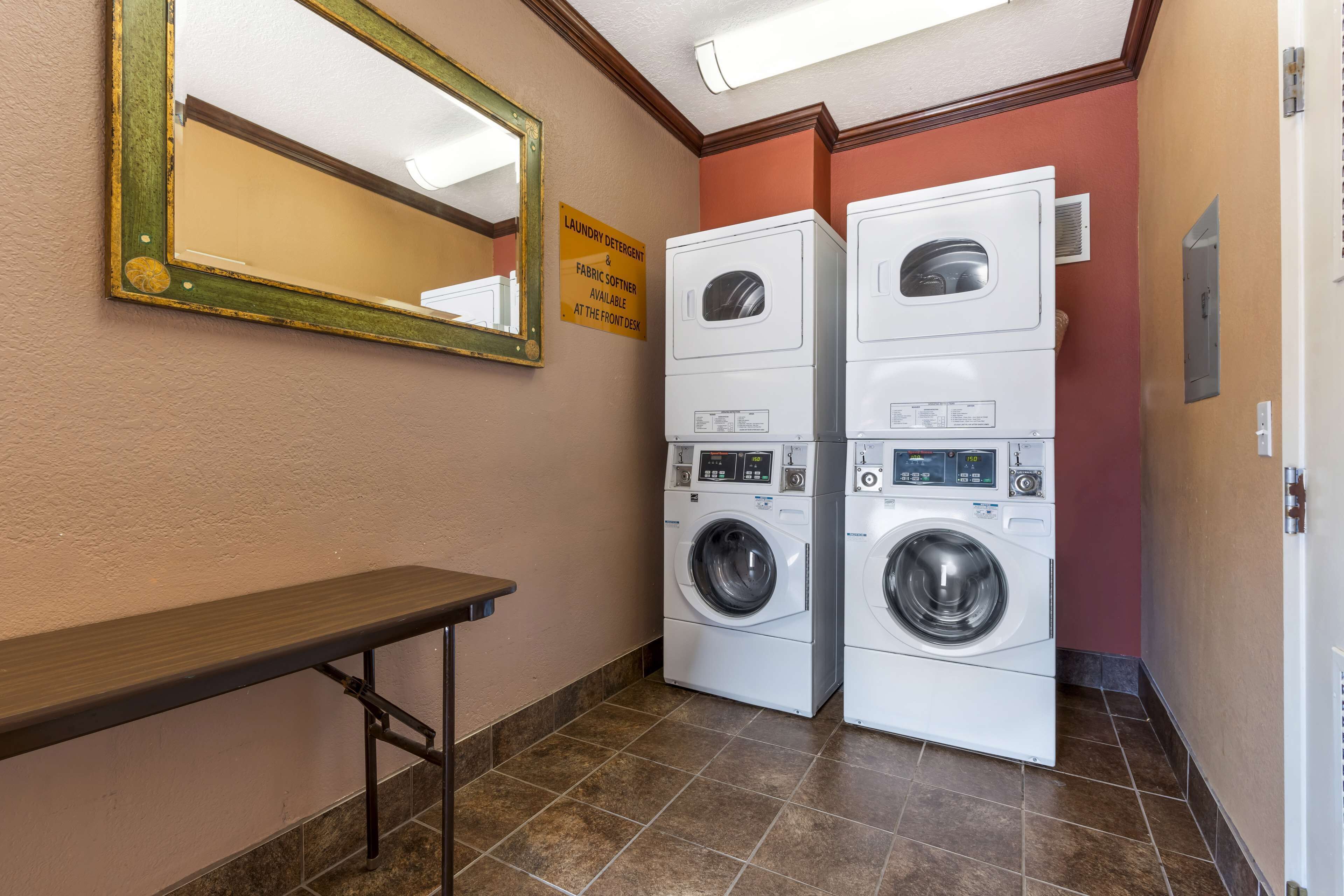 A laundry room with two stacked washers and dryers, a bench, and a sign indicating laundry detergent and fabric softener availability.