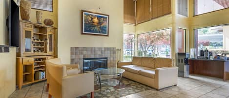 Amplia sala de estar con sofá, mesa de centro de vidrio y chimenea. Se observa una cocina con cafetera y mostrador.