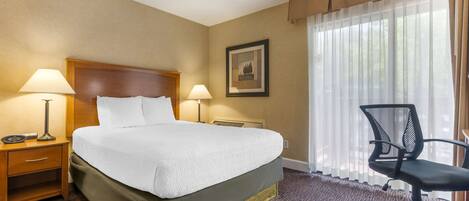 Habitación de hotel con una cama grande, dos lámparas de noche, un escritorio con silla y una ventana con cortinas traslúcidas.
