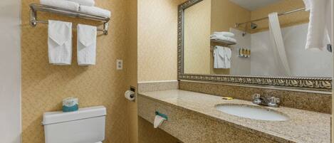 A bathroom with a toilet, sink, and mirror. There are towels on a rack and a shower curtain.
