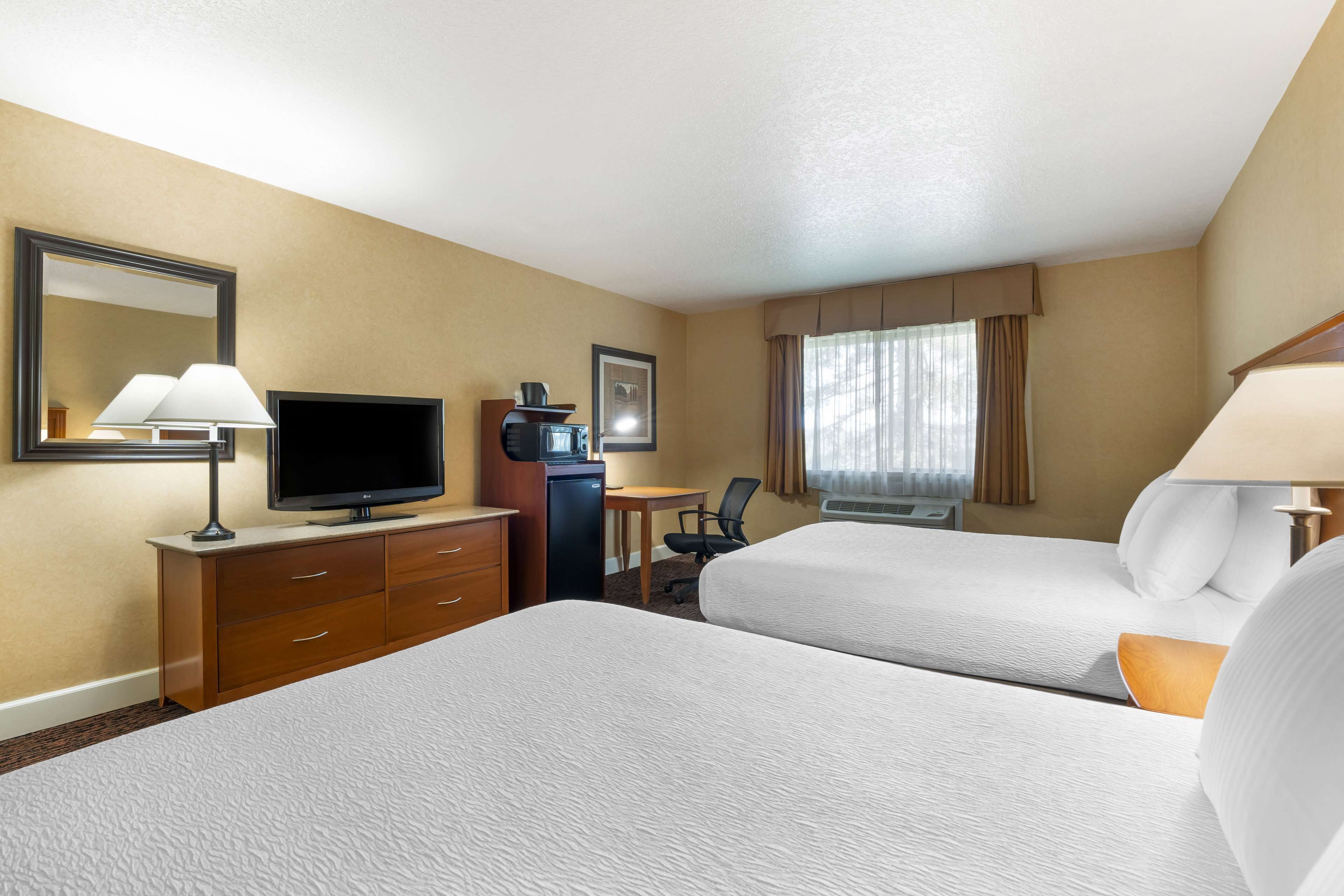 A hotel room with two beds, a desk with a computer, a television, and a mirror.