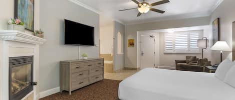 Habitación de hotel con una cama grande, un televisor montado en la pared, chimenea, ventilador de techo y ventana con persianas.