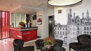 Un espace d’accueil avec un comptoir rouge, des chaises noires à motifs, une grande fresque murale et un projecteur au plafond.