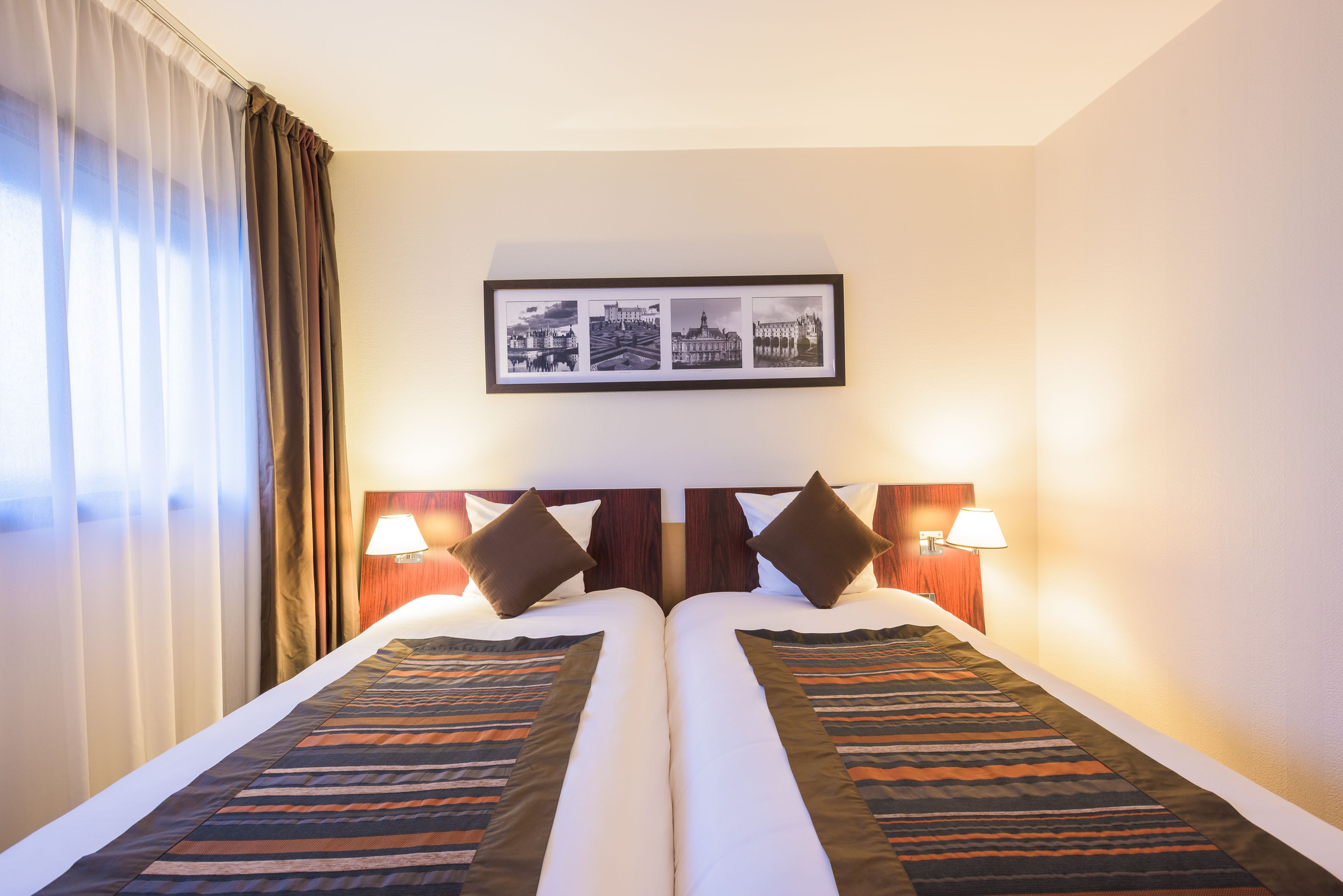 A hotel room with two beds, a framed picture of cityscapes, and two bedside lamps.