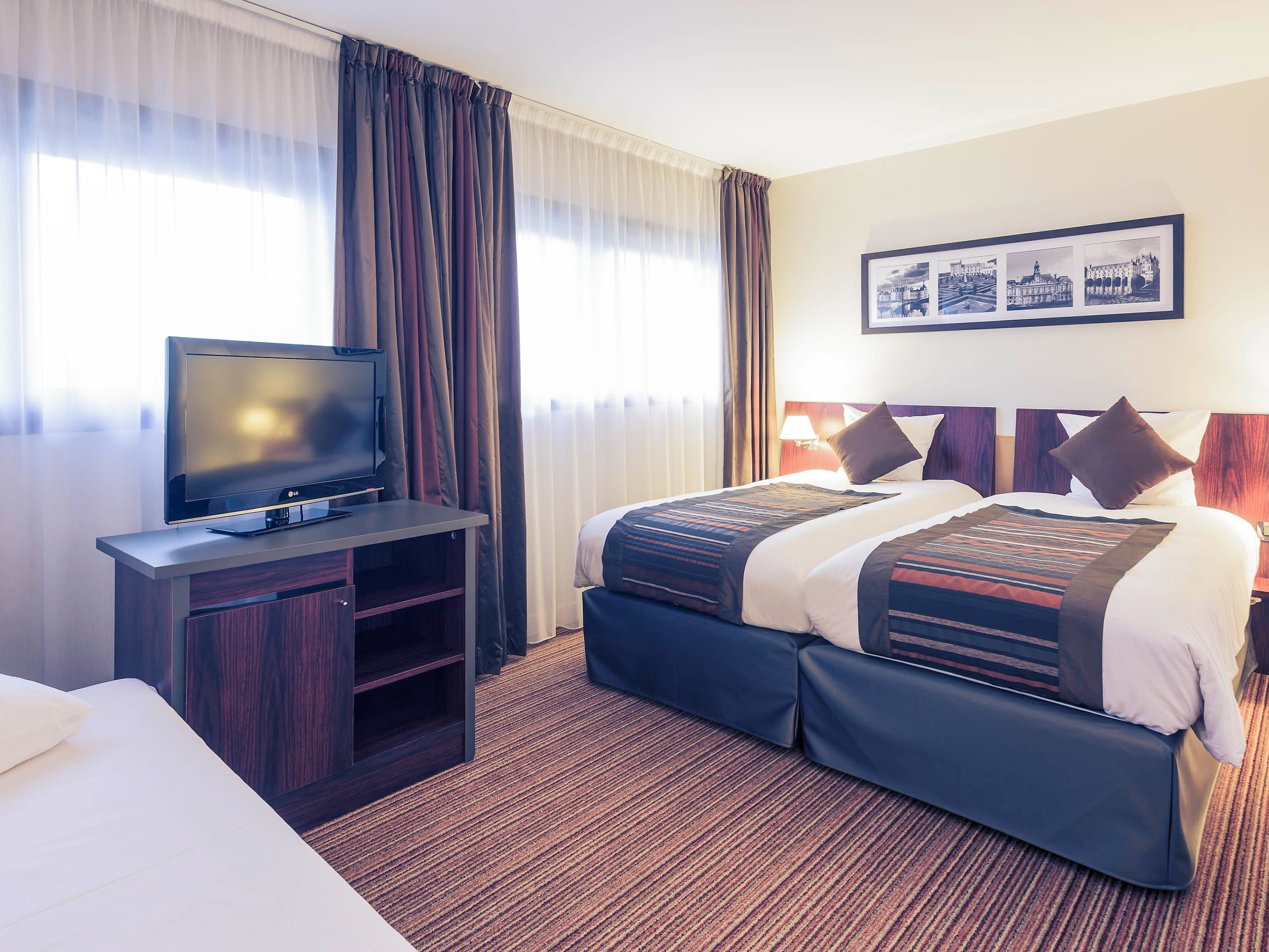 A hotel room with a bed, a TV on a wooden stand, and a framed picture on the wall.