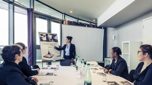 Une salle de conférence équipée d’un écran de présentation, d’un projecteur, et où les participants sont assis autour d’une table, chacun ayant devant soi une bouteille d’eau et des documents.