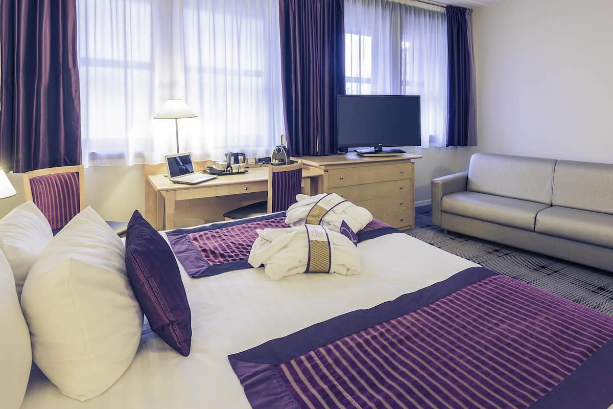 Een hotelkamer met een bed, een bureau, een televisie, een bank en gordijnen.