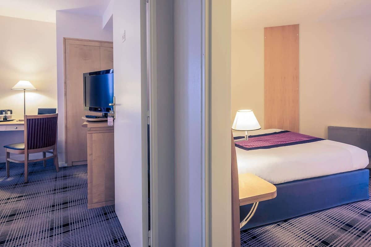 Een hotelkamer met een bed, bureau, stoel, televisie en lamp.