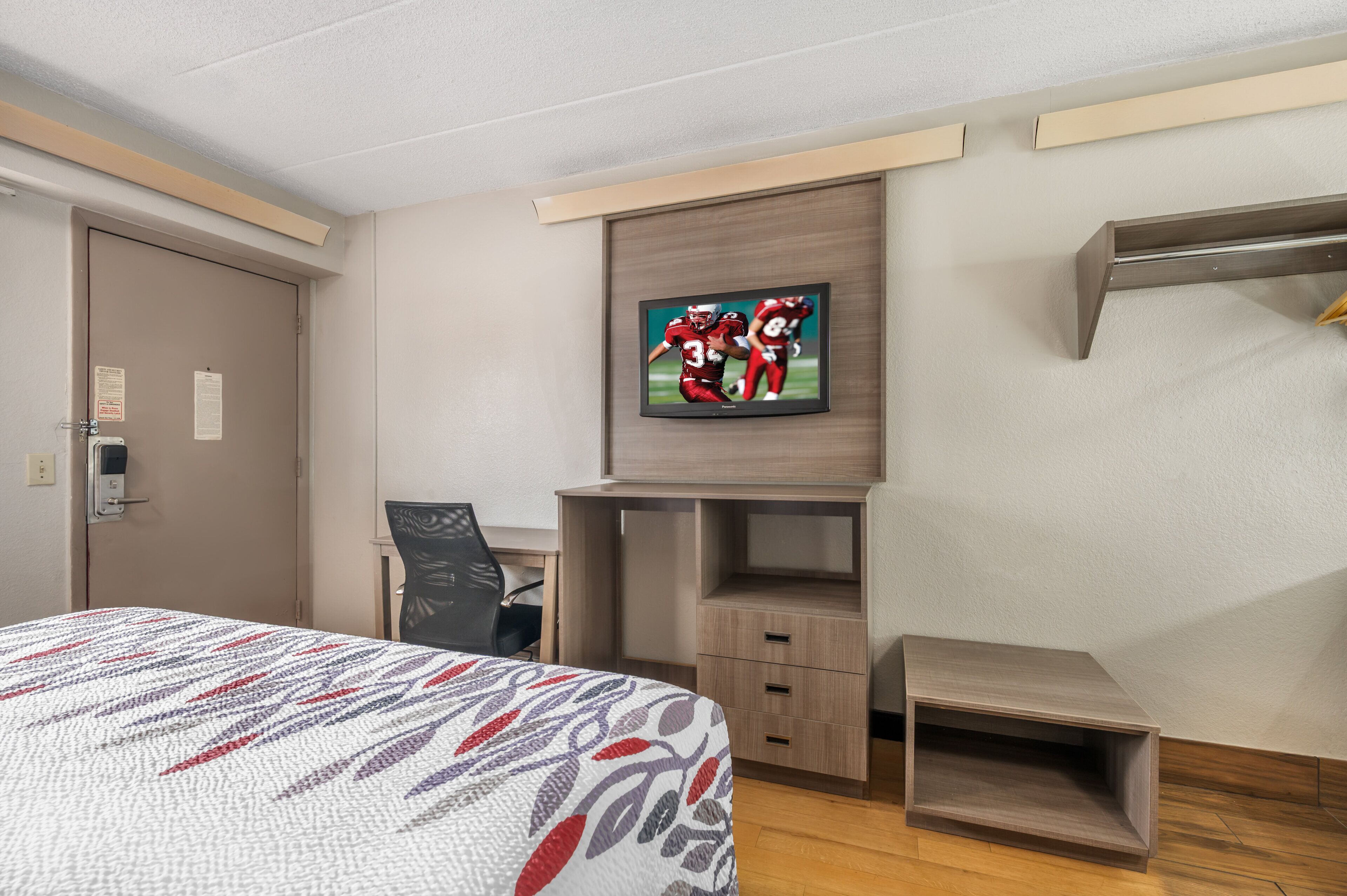 Habitación de hotel con una cama, un escritorio, una silla, un televisor montado en la pared y un armario.
