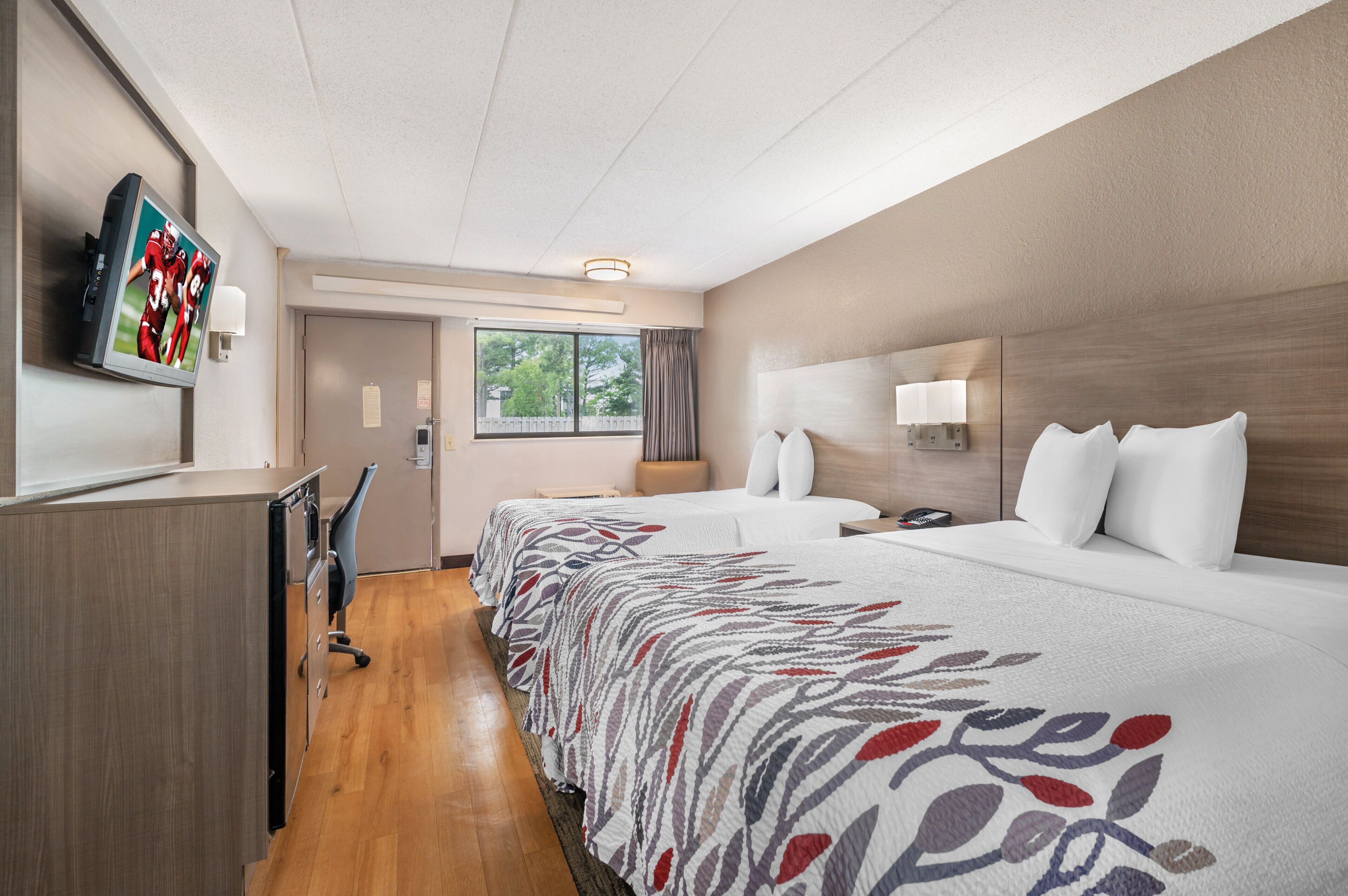 A hotel room with a bed, bedside table, lamp, and a television mounted on the wall.