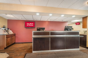 Uma área de recepção com balcão, máquina de café e aviso indicando Wi-Fi gratuito em todos os quartos.