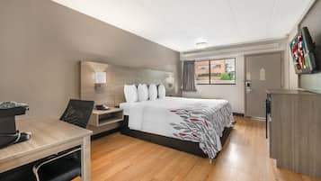 Habitación de hotel con cama, escritorio, silla, televisor y ventana con cortinas.