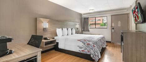 A hotel room with a bed, desk, chair, TV, and a window with curtains.
