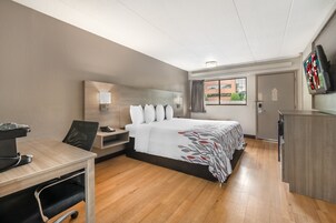 Habitación de hotel con cama, escritorio, silla, televisor y ventana con cortinas.