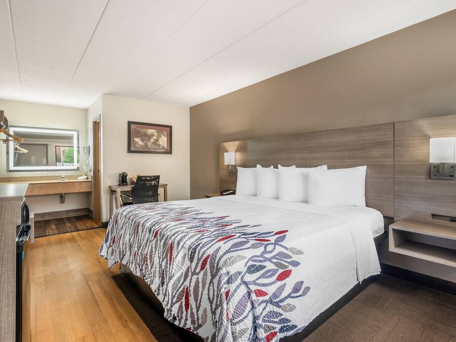 Quarto de hotel com uma cama grande, uma escrivaninha com cadeira, um espelho e uma televisão fixada na parede.