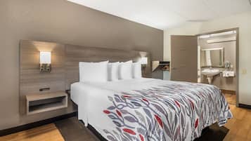 Ein Hotelzimmer mit einem Bett, Nachttischlampen, einem Nachttisch, einem Spiegel und einem Badezimmer mit Waschbecken und Spiegel.