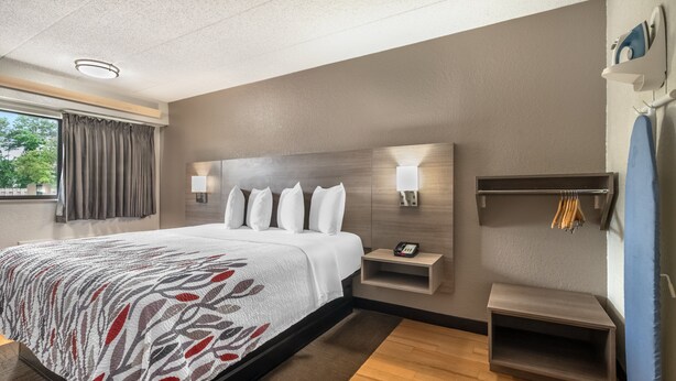 A modern hotel room with a large bed, bedside lamps, a small bedside table, and a built-in shelf. - Red Roof Inn Virginia Beach (Virginia Beach)