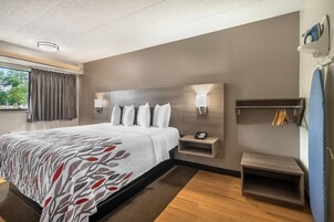Una habitación de hotel moderna con una cama grande, lámparas de noche, una mesita de noche pequeña y una estantería empotrada.