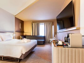 Una habitación de hotel con una cama grande, un sofá, una cafetera y un televisor.