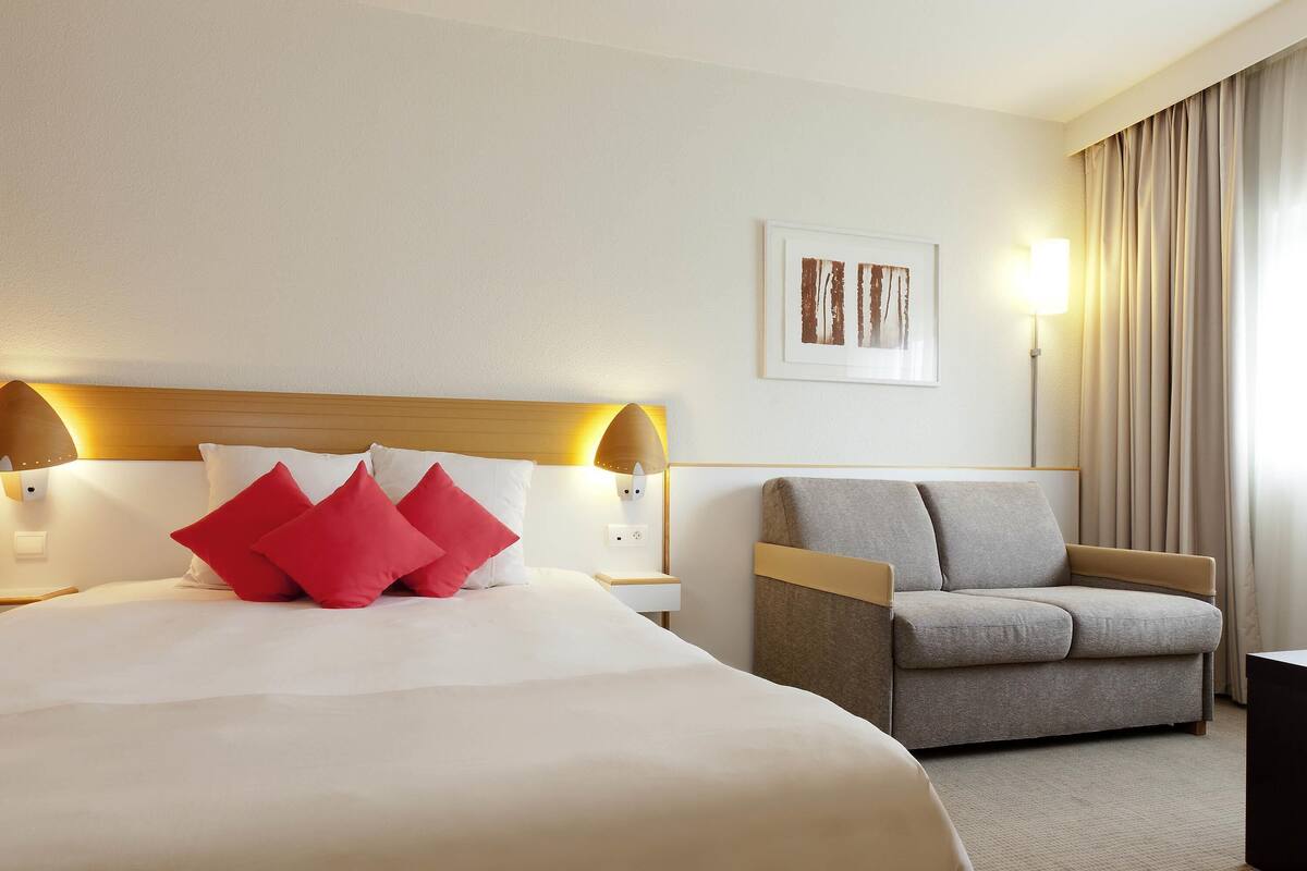 Een hotelkamer met een bed, een slaapbank, een lamp en een schilderij aan de muur.