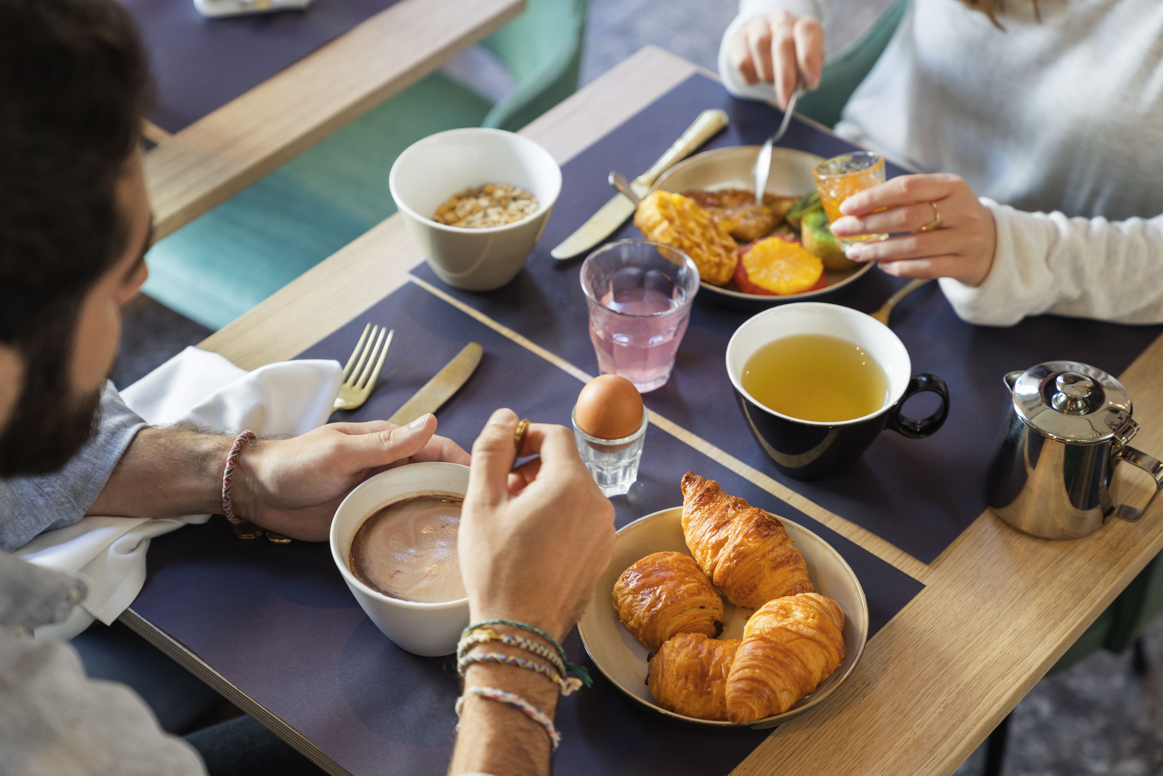 Une table à manger avec des aliments pour le petit-déjeuner, notamment des croissants, un bol de soupe, une assiette de fruits, un verre de jus de fruits et une cafetière.