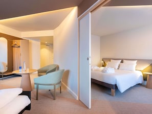 A hotel room with a bed, a chair, a small table, and a wardrobe.