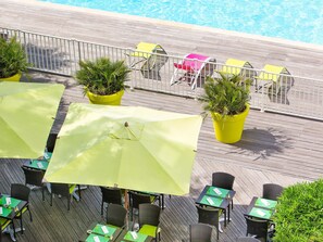 A poolside area with outdoor seating, including tables and chairs, and potted plants.
